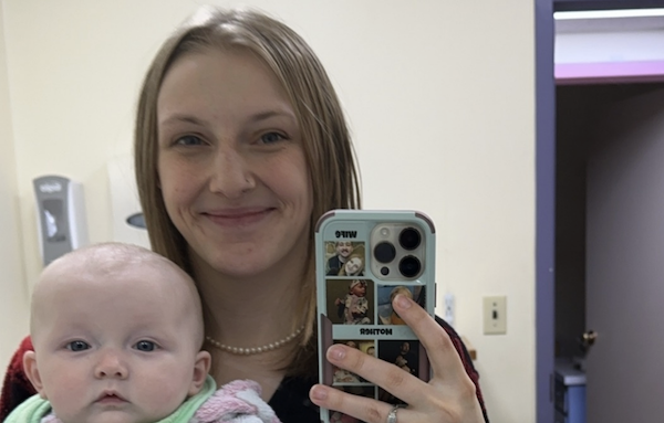 Mother and baby pose together for a mirror photo, with the woman’s phone case featuring several small personal photos.