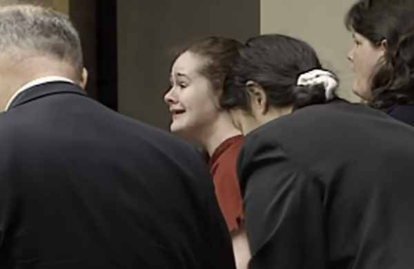 Four people, including a visibly upset woman in red, are gathered, possibly during a tense legal proceeding or court hearing.