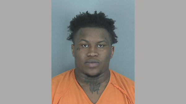 Police custody image of a man dressed in orange prison clothing, taken against a plain, light-colored wall.