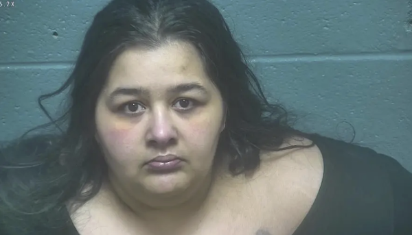 Close-up of a woman with pale skin and dark hair during intake, seated against a painted concrete background.