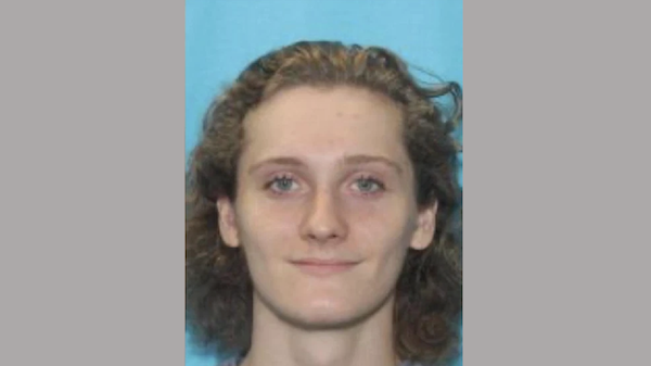 Identification-style photo of an individual with medium-length hair and clear skin, facing forward in front of a bright blue background.