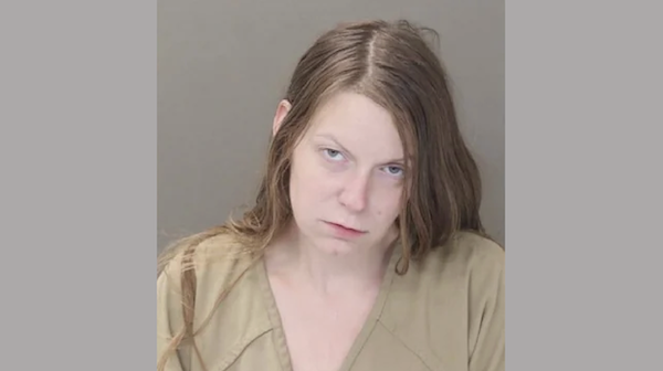Portrait of a woman with loose, shoulder-length hair dressed in khaki jail clothing, shown in a booking photo.