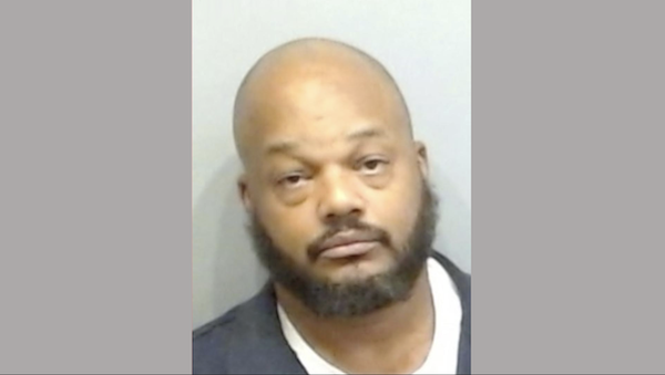 Police photo of a man with a bald head and black beard, facing forward with a subdued expression.