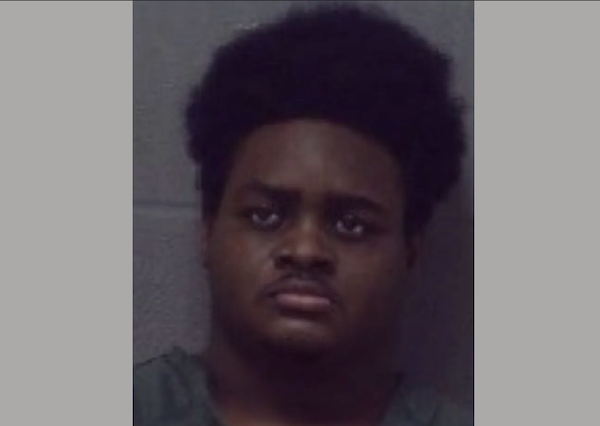 Portrait-style mugshot featuring a man with a neutral expression, dark curly hair, and a plain gray background.