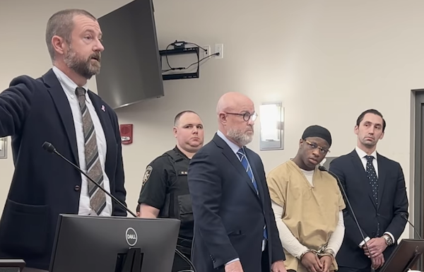 A group including a handcuffed defendant, two lawyers, a law enforcement officer, and a man giving a statement is pictured during court proceedings.