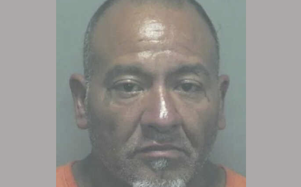 Portrait-style mugshot of a man looking directly at the camera, with a tan complexion, visible forehead shine, and an orange shirt.