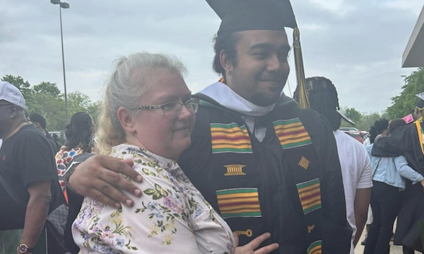 Graduate and family member stand together outside, both smiling, surrounded by fellow attendees at a graduation gathering.