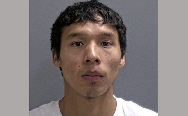 Head-and-shoulders image of a serious-looking individual with tousled hair and a smooth complexion, set against a solid gray background.