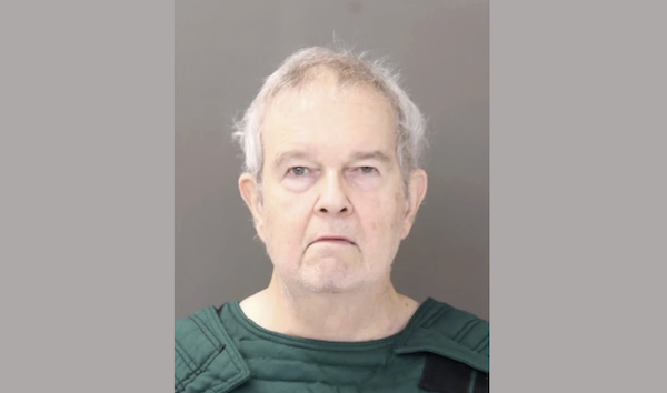 Middle-aged to elderly man in a green padded vest, photographed head-on with a flat, neutral background, exhibiting no visible emotion.