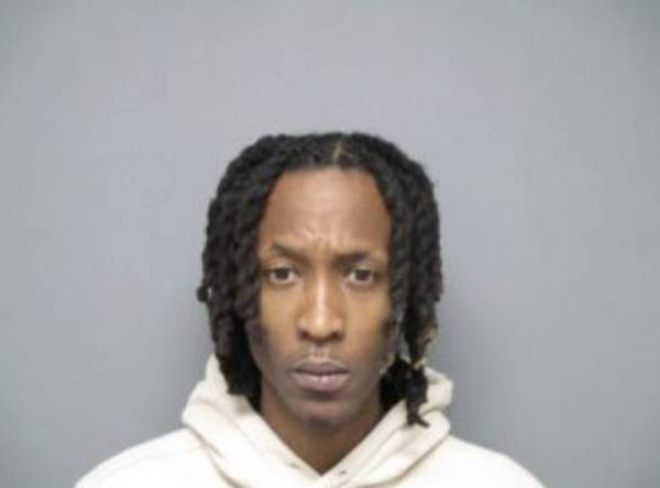 Photo of a man in a white hoodie with shoulder-length braids, shown from the shoulders up with a serious facial expression.