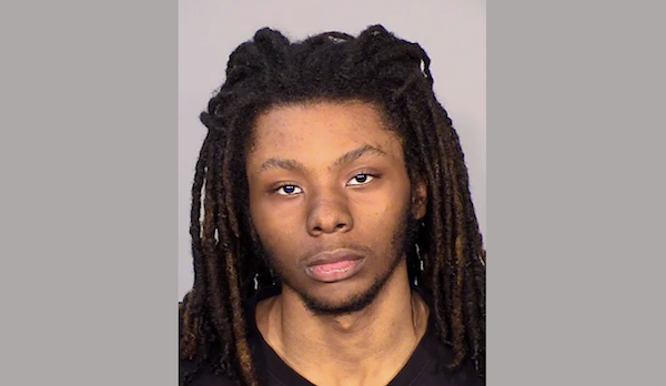 Mugshot image featuring a young man looking directly at the camera with a serious expression, his hair styled in long dreadlocks against a light gray background.