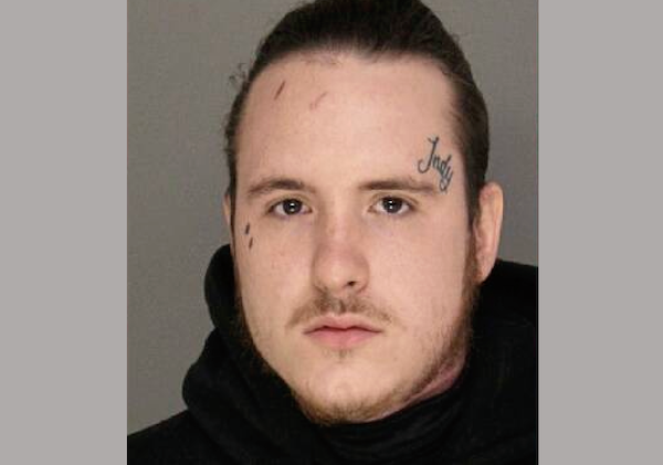 Arrest photo featuring a male subject with tied-back hair, visible facial tattoos, and a direct gaze, set against a gray background with no objects or accessories visible.
