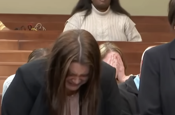 Courtroom image showing a woman overcome with emotion in the front, while a person seated behind her hides their face, suggesting distress or shock during proceedings.