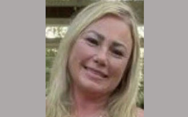 Smiling blonde woman posing for a photo outside, with her head slightly tilted and natural light illuminating her face.