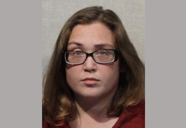 Close-up image of a woman in a red garment with glasses, looking directly at the camera with a neutral facial expression.