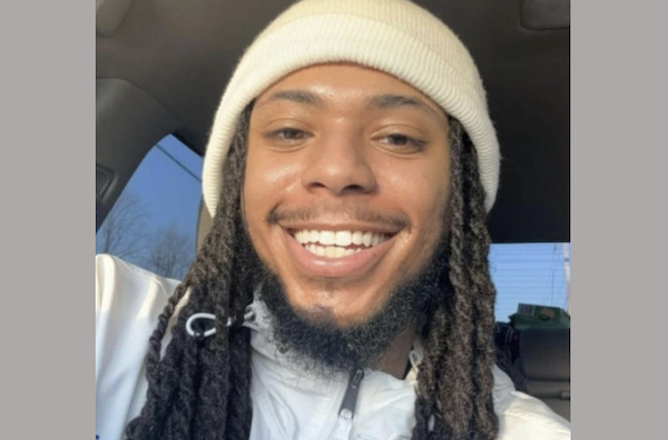 Close-up image of a cheerful person with long hair in locs, sporting a cream knit beanie and casual jacket, inside an automobile.