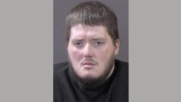 Arrest photo featuring a light-skinned man with short, dark hair and facial hair, dressed in black, set against a monotone background.