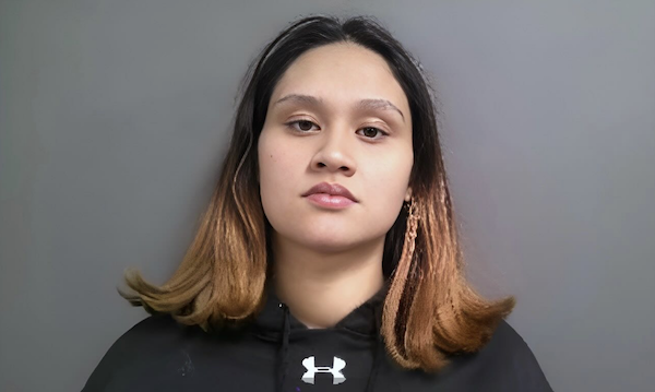 Woman in a black athletic hoodie and two-tone brown hair, gazes forward with a calm demeanor, neutral background behind her.
