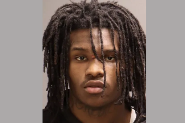 Headshot of a man with prominent dreadlocks and a serious demeanor, photographed for identification purposes with a neutral gray background.