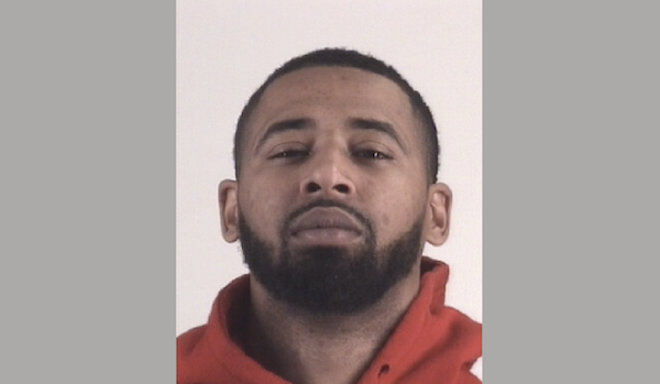 Portrait-style image of a man with dark facial hair and a red pullover, photographed against a simple, pale backdrop.