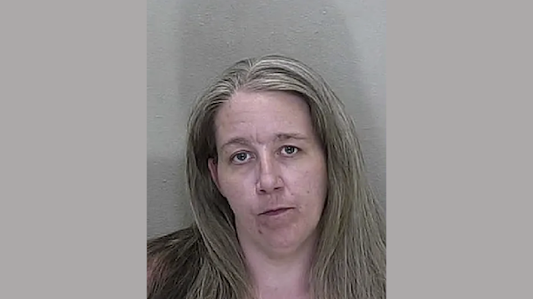 Headshot image of a woman with visible blemishes and straight hair, looking directly into the camera with a serious expression.