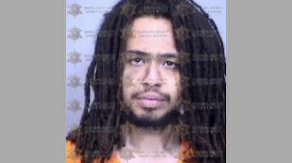 Close-up image of a man’s face with shoulder-length dreadlocks and a faint beard, pictured in an orange top, with official watermarking from a sheriff’s department.
