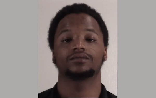 Close-up image of a young man in a black shirt, facing forward in a simple, softly lit setting.