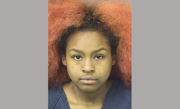 Headshot of a young woman with fluffy, orange-tinted hair, facing forward against a simple, light background.