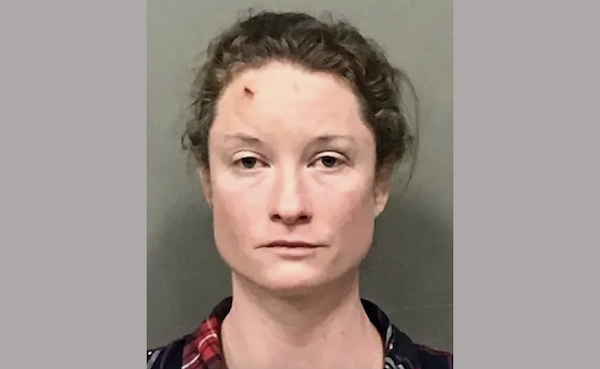 Front-facing mugshot of a woman with loosely tied-back hair and a mark on her forehead, photographed against a neutral background.