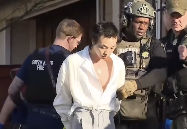 Deputies in helmets and body armor escort a handcuffed man outdoors in daylight, with one officer pointing off frame.