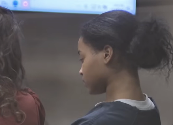 A woman with her hair tied back sits next to a lawyer during a courtroom proceeding.