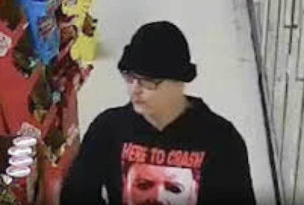 Grainy indoor image of a person in dark clothing looking to the side near a retail display.