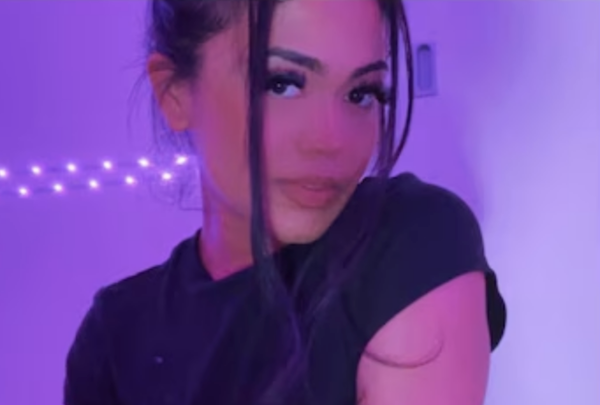 Woman photographed in moody violet lighting, turning slightly toward the camera in a black top, with illuminated fairy lights creating a soft backdrop.