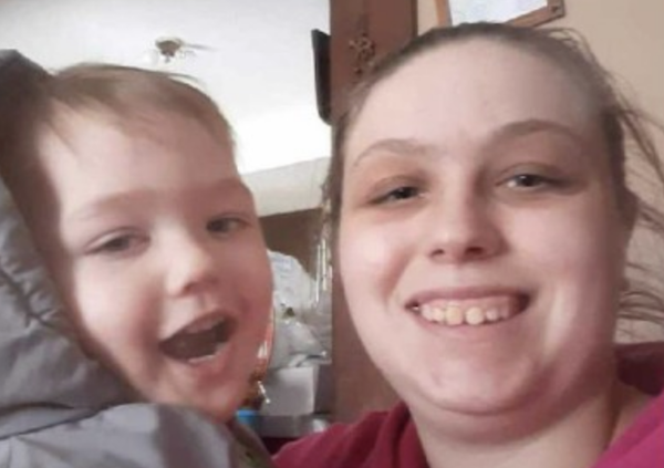 A child with an open-mouthed smile poses next to a smiling woman in a pink hoodie.