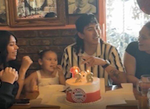 People sit together at a dining table during a birthday celebration, with a child seated near the cake.