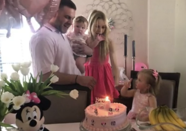 Birthday party scene with a young girl, two adults and a baby gathered around a cake.