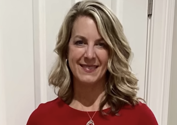 Woman with wavy blonde hair and a necklace poses for a clear indoor portrait.