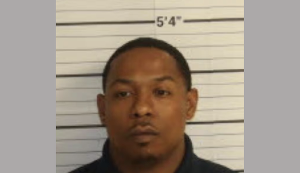 1. Police booking-style portrait of a man with closely cropped hair and a small goatee, positioned against a height marker.