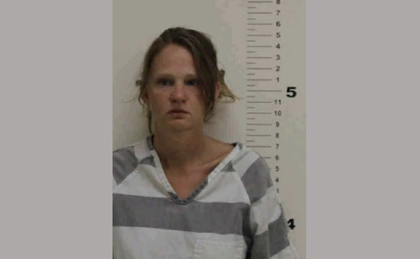 Head-and-shoulders mugshot of a woman with loosely tied-back hair in a gray striped uniform beside height markers.