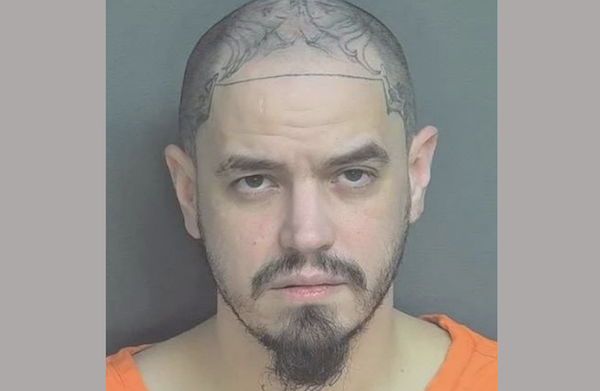 1. Police booking-style portrait of a tattooed man with a closely shaved head and trimmed beard, photographed against a plain gray backdrop.